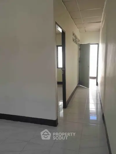 Bright hallway with open door leading to sunlit room, showcasing sleek tiled flooring and modern design.