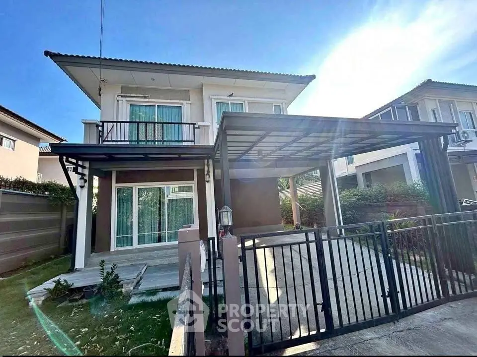 Modern two-story house with gated driveway and balcony in a sunny suburban neighborhood.