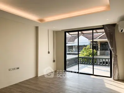 Spacious living room with large windows and balcony access, featuring modern lighting and wood flooring.