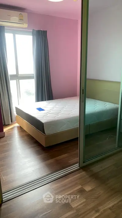 Spacious bedroom with large window and wooden flooring in modern apartment.