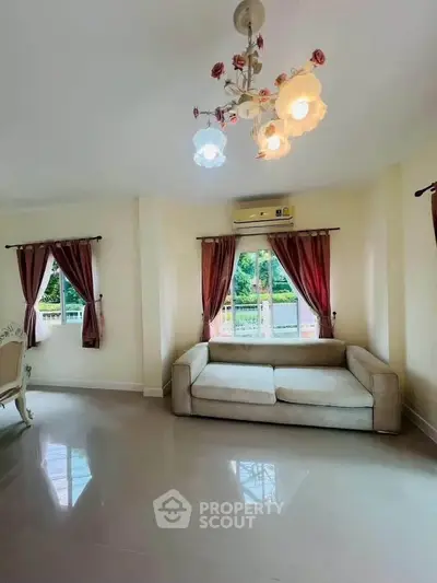 Spacious living room with elegant chandelier and cozy sofa, featuring large windows with lush garden view.