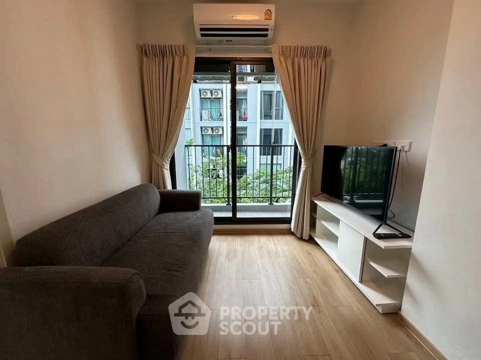 Cozy living room with modern sofa, TV, and balcony view in urban apartment.