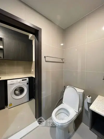 Modern bathroom with adjacent laundry area featuring a washing machine, sleek design and neutral tones.