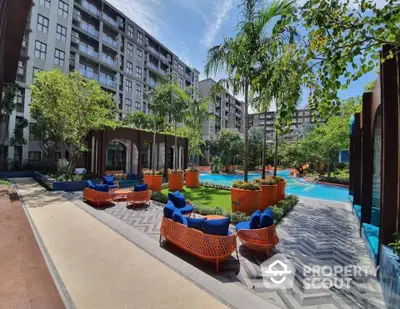 Luxurious apartment complex with lush garden and poolside seating area.