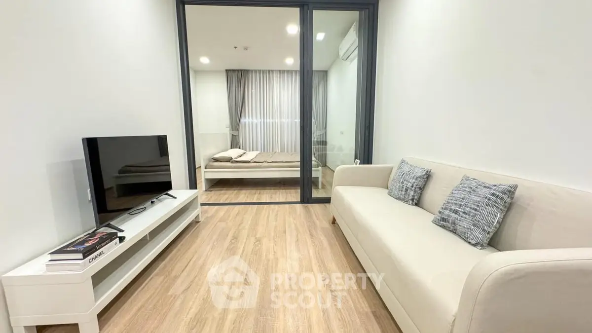 Modern living room with cozy sofa and TV, adjacent to a stylish bedroom with glass partition.