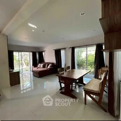 Spacious living room with large windows and garden view, featuring modern furniture and ample natural light.