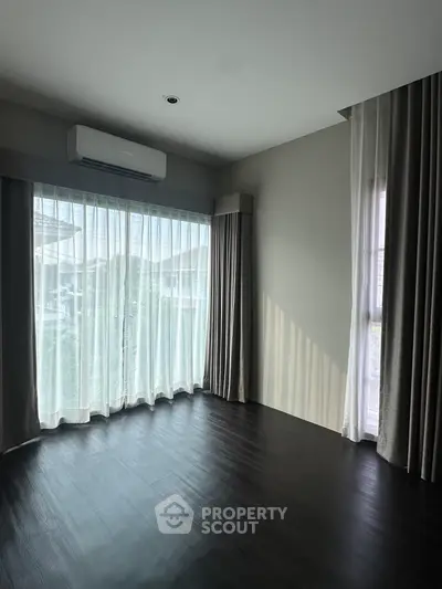 Spacious empty room with large windows and dark wood flooring, perfect for customization.