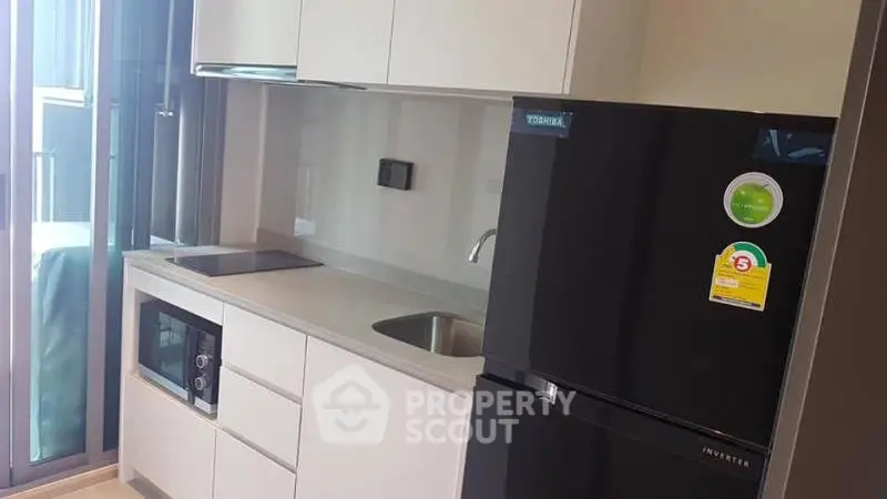 Modern kitchen with sleek cabinetry, built-in microwave, and black refrigerator in a compact layout.