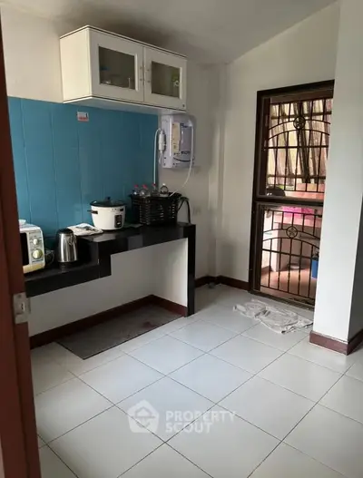 Compact kitchen with modern appliances and blue backsplash, featuring a sleek countertop and tiled floor.