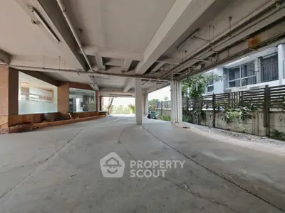 Spacious covered parking area in modern residential building with natural light and greenery.