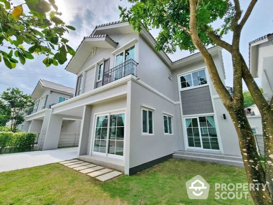 Modern two-story house with lush green lawn and large windows in a serene neighborhood.