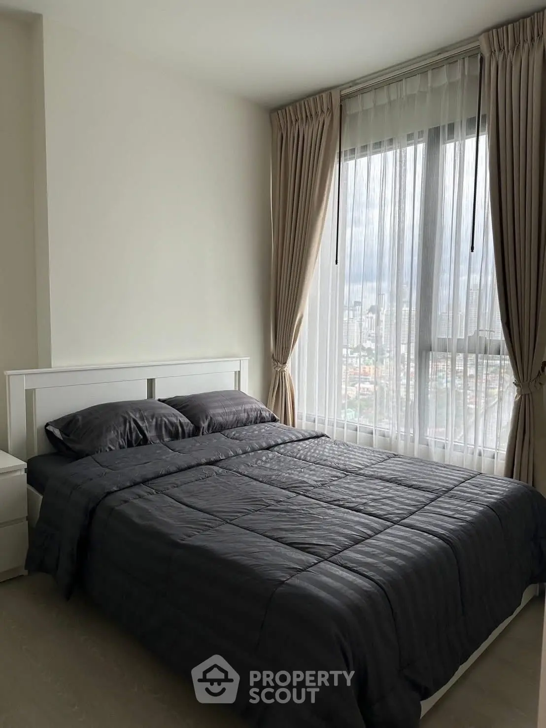 Modern bedroom with large window and city view, featuring elegant curtains and sleek bedding.