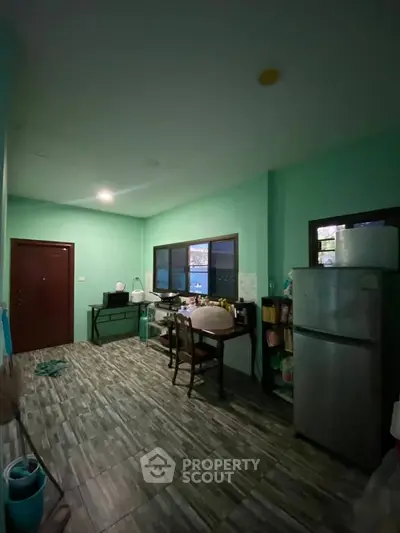 Cozy kitchen with green walls and dining area, featuring a fridge and ample natural light.