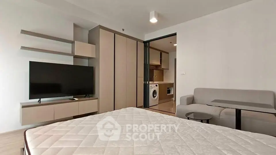 Modern studio apartment with sleek design, featuring a cozy living area, built-in shelves, and a compact kitchen.