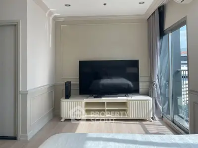 Modern bedroom with large TV and balcony view, featuring elegant decor and natural light.