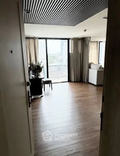 Spacious living room with large windows and city view, featuring elegant wooden flooring.