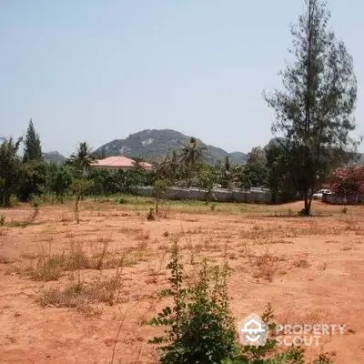 Expansive undeveloped land with rich red soil, set against a backdrop of lush greenery and distant hills, offering a serene and picturesque setting for a bespoke residential or commercial development.