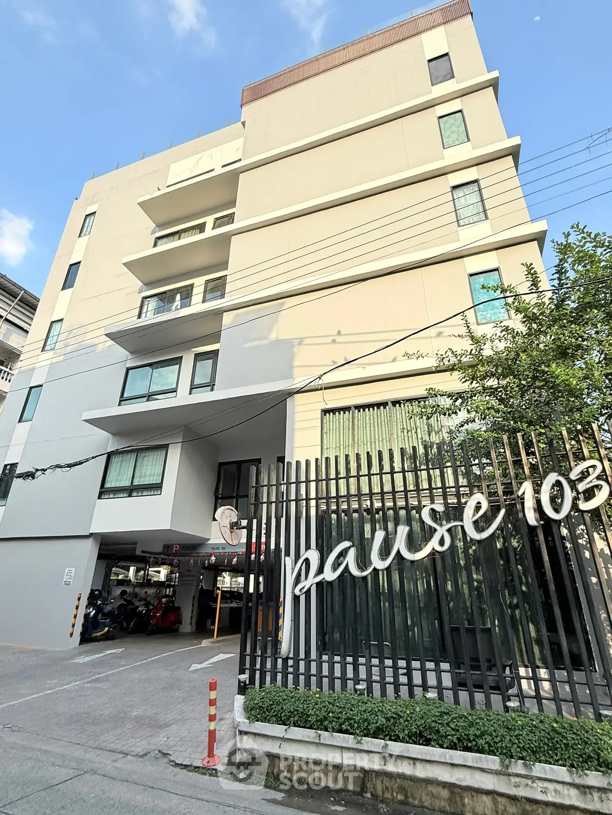 Modern multi-story residential building with gated entrance and parking area.