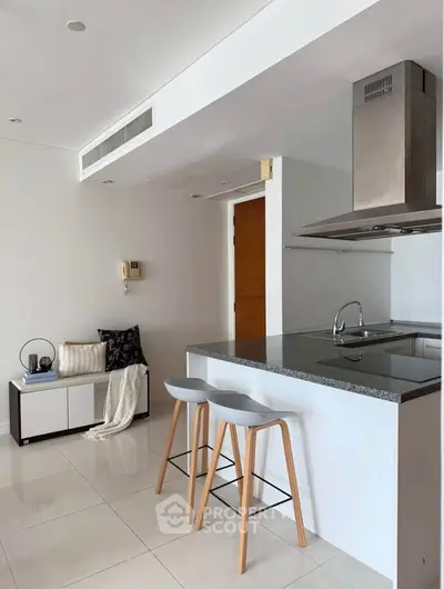 Modern kitchen with sleek island and bar stools in a bright, minimalist apartment.