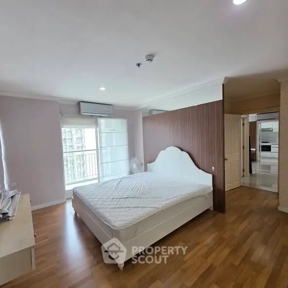 Spacious bedroom with wooden flooring and large windows in modern apartment.