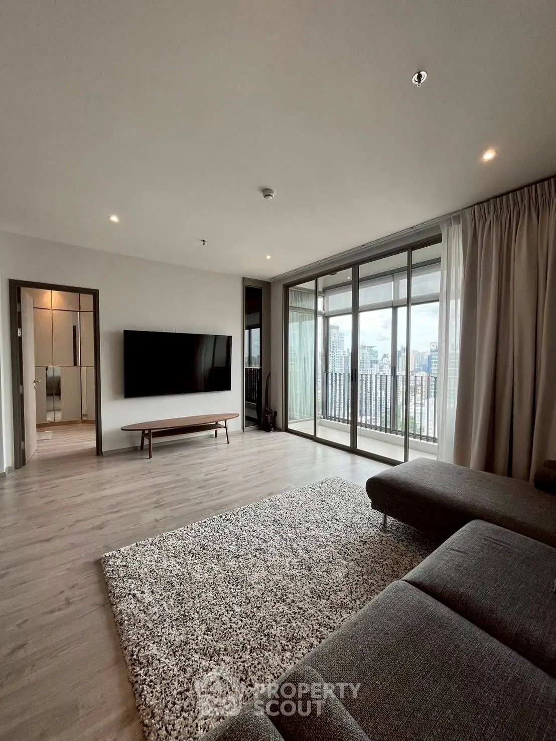 Spacious modern living room with large windows and city view, featuring sleek furniture and elegant decor.