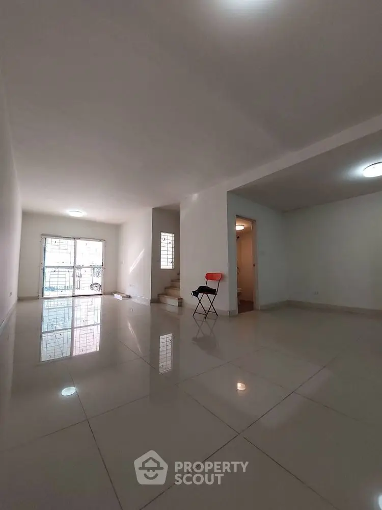 Spacious empty living room with glossy tiled floors and natural light.