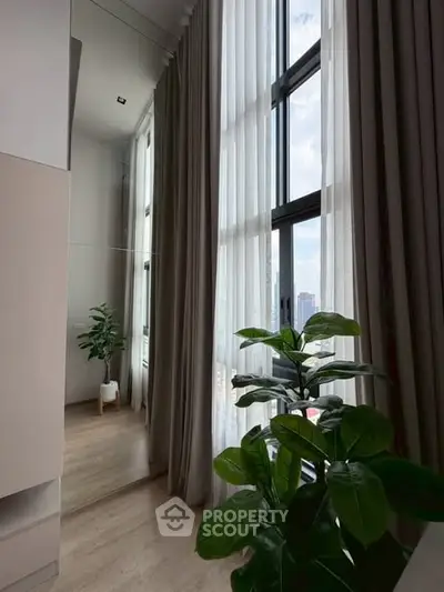 Elegant high-ceiling room with large windows and lush indoor plants, offering a serene and airy ambiance.