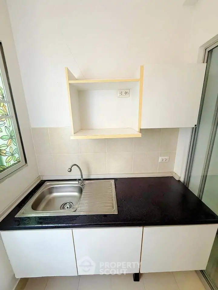 Modern kitchen with sleek black countertop and stainless steel sink, featuring minimalist white cabinetry.