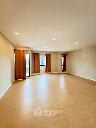 Spacious empty living room with wooden flooring and large windows.