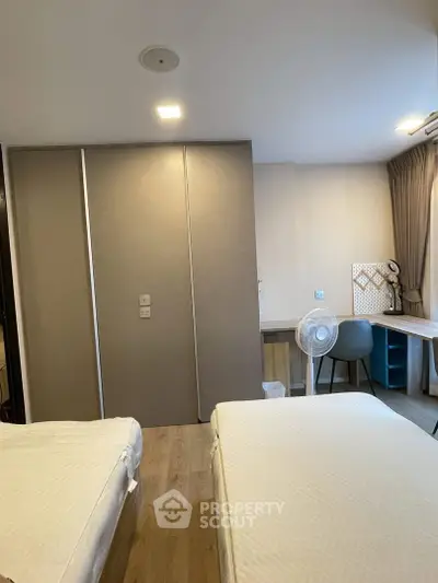 Modern bedroom with twin beds and study area, featuring sleek design and ample natural light.