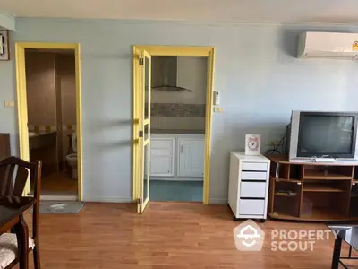 Spacious living room with classic wooden flooring, bright yellow doors, and traditional furniture, leading to a cozy kitchen area.