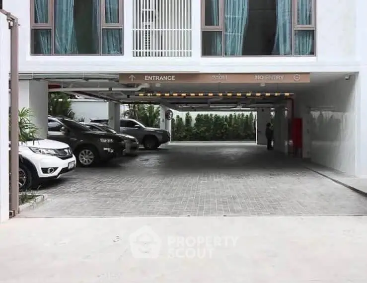 Modern building entrance with spacious parking area and multiple vehicles.