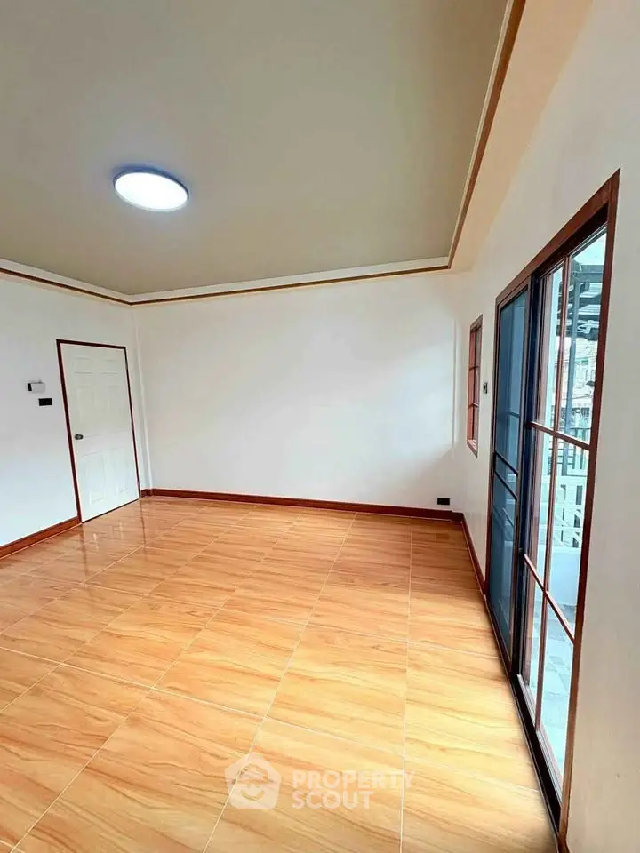 Spacious empty room with wooden flooring and large windows, perfect for customization.