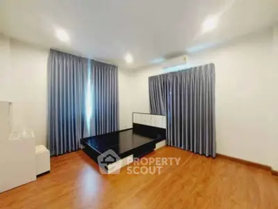 Spacious bedroom with modern design and wooden flooring, featuring large windows with elegant curtains.
