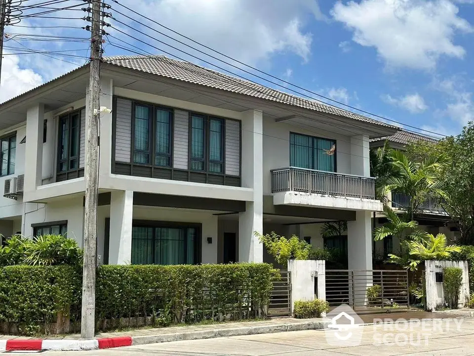 Modern two-story house with balcony and lush greenery in a serene neighborhood.