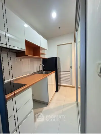 Modern kitchen with sleek cabinetry and compact design, featuring a black fridge and wooden countertops.