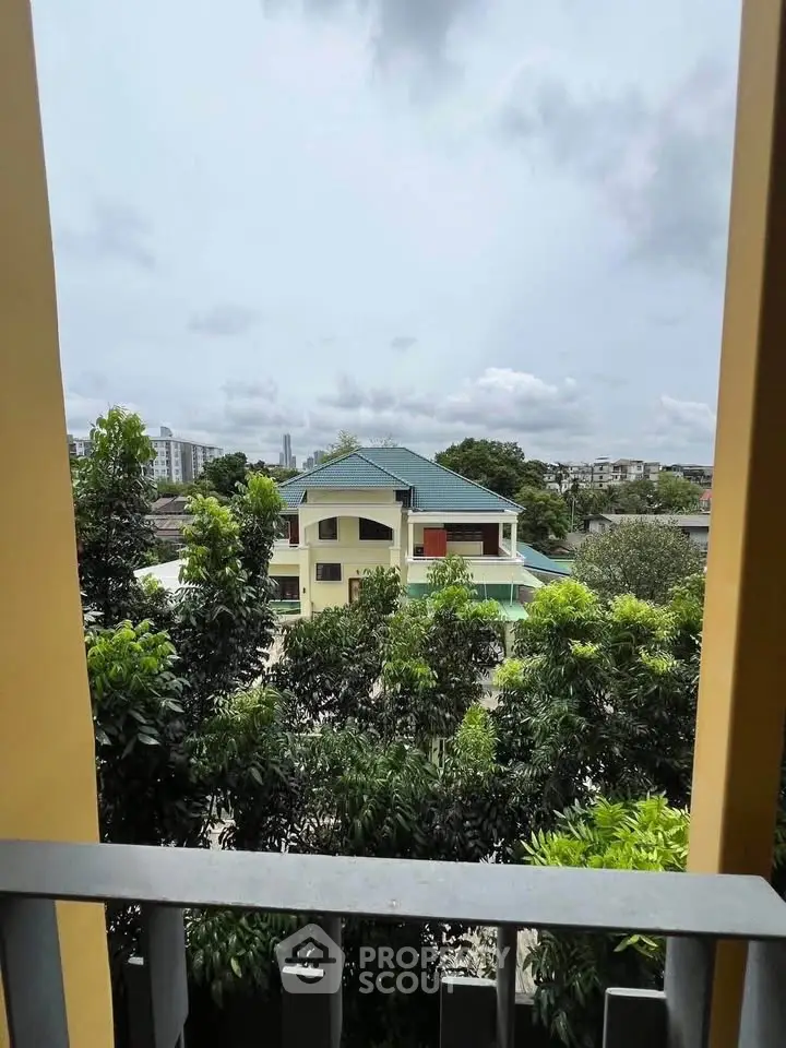 Scenic view from balcony overlooking lush greenery and a charming house with a green roof.