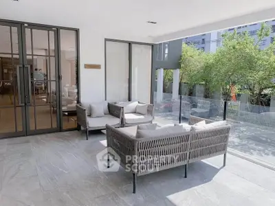 Modern balcony with stylish outdoor seating and glass railing, offering a serene view of lush greenery.