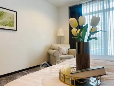 Cozy bedroom with elegant decor and natural light, featuring a plush armchair and stylish vase centerpiece.