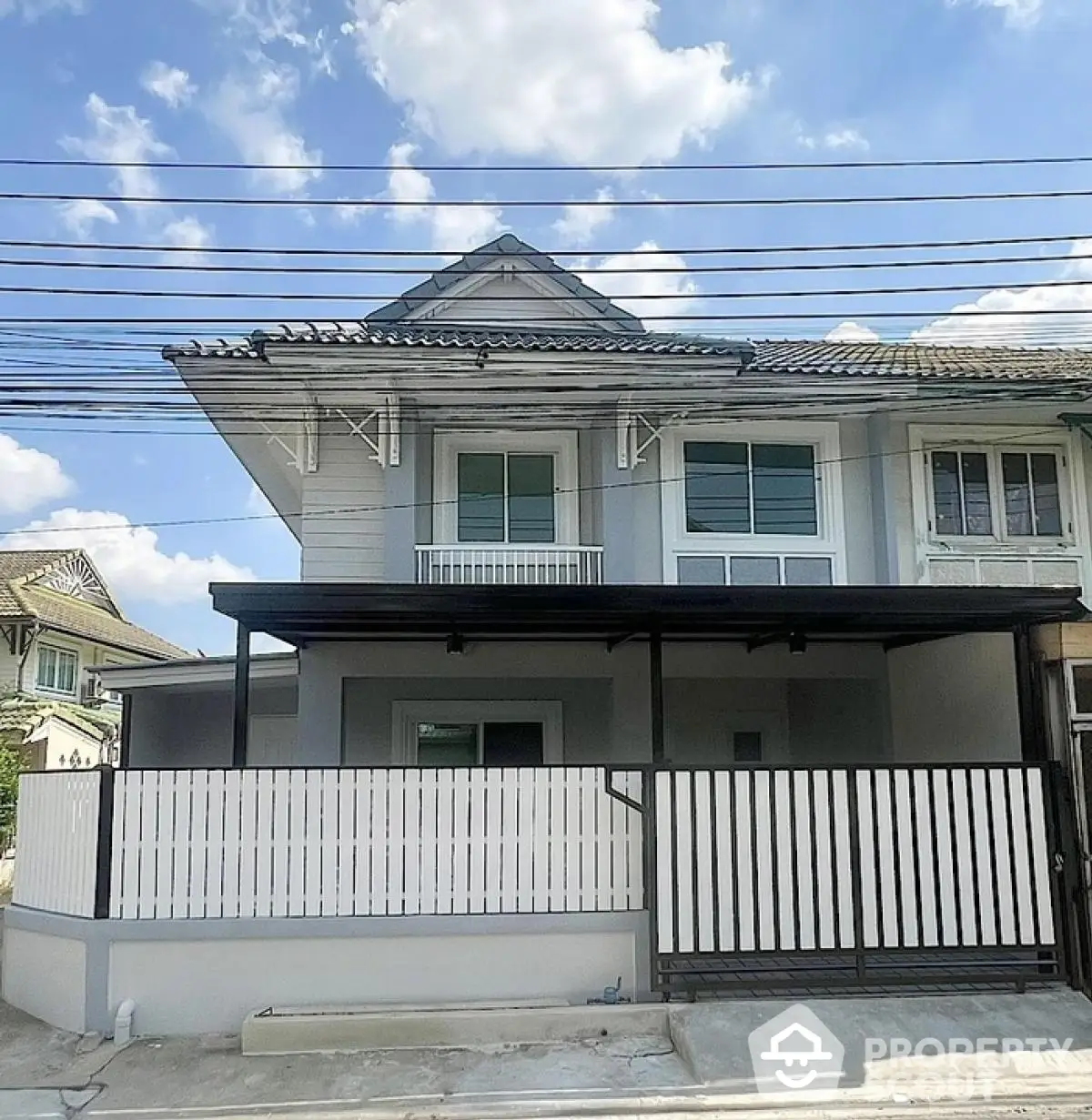 Charming two-story townhouse with modern facade and fenced front yard under a clear blue sky.