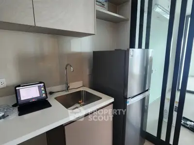 Modern kitchen with sleek design, featuring stainless steel fridge and built-in sink.