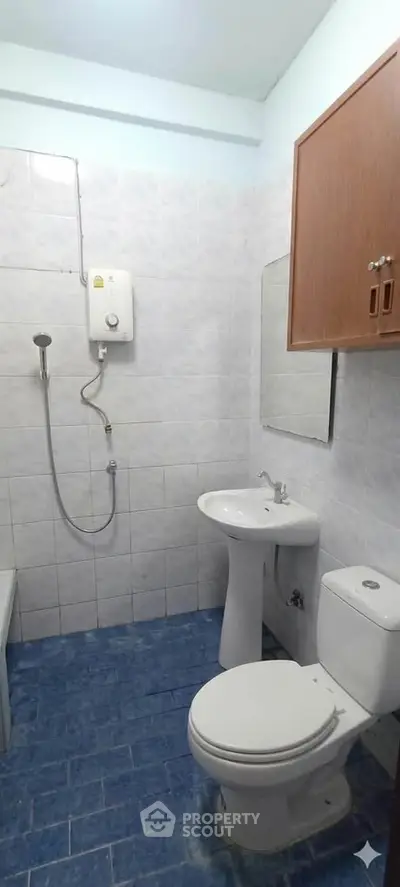 Compact bathroom with shower, toilet, and sink in a tiled setting.