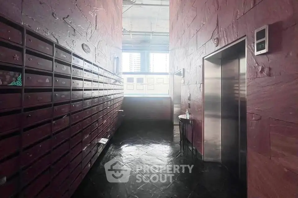 Modern building lobby with mailboxes and elevator, featuring sleek design and natural lighting.