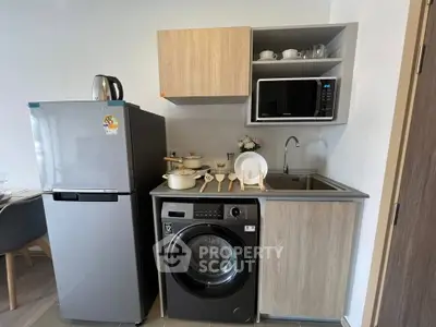 Modern compact kitchen with washing machine, fridge, and microwave in stylish apartment.
