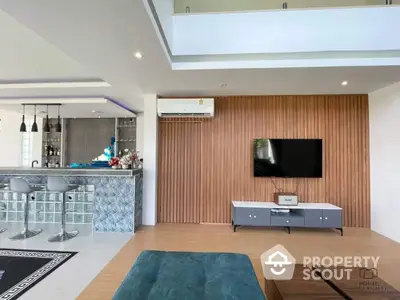 Spacious modern living room seamlessly connects to an open layout kitchen with bar seating, featuring sleek furnishings and a warm wooden accent wall.