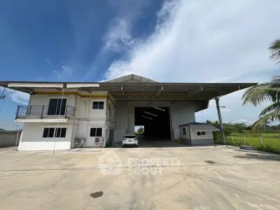 Spacious warehouse with attached office and ample parking space under clear blue skies.