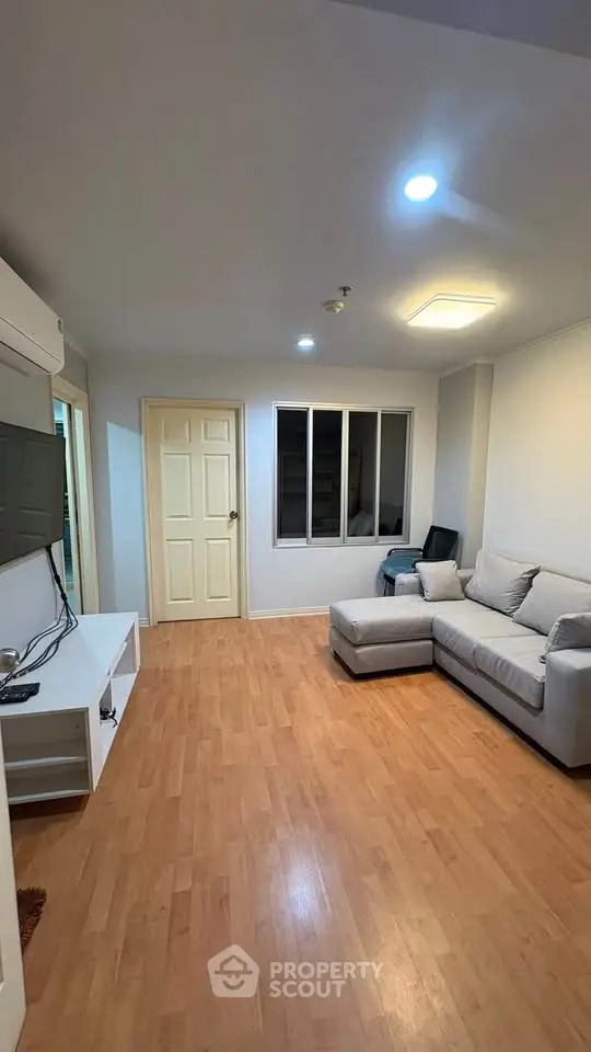 Spacious living room with modern decor and wooden flooring, featuring a cozy sofa and wall-mounted TV.