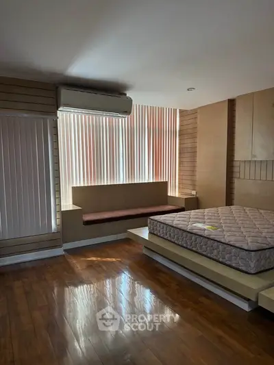 Spacious bedroom with wooden flooring and natural light, featuring a built-in bench and air conditioning.