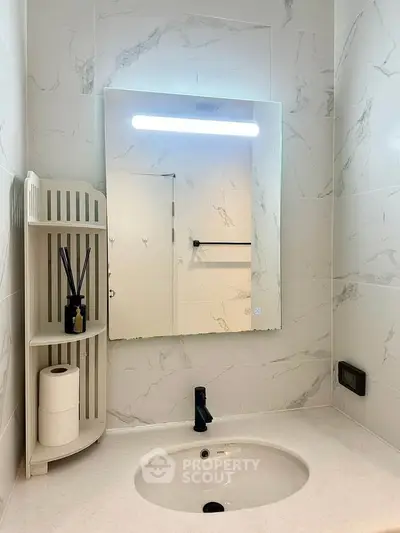 Modern bathroom with sleek vanity and illuminated mirror, featuring elegant marble tiles.