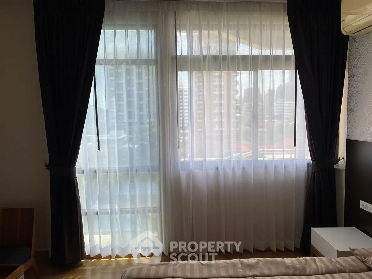 Modern bedroom with large windows and city view, featuring elegant curtains and air conditioning.